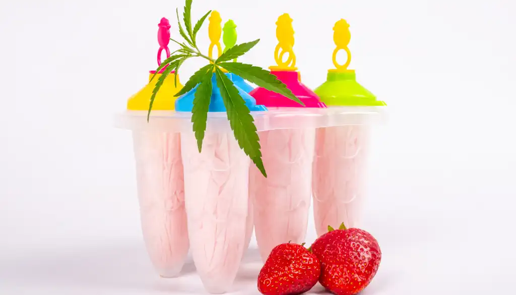 Ein eleganter Becher voll cremigem Erdbeereis, sanft durchzogen von CBD-Öl, das in feinen, glänzenden Streifen die Oberfläche verziert. Frische, reife Erdbeeren sind kunstvoll um das Eis arrangiert, ihre lebendige rote Farbe harmoniert perfekt mit den zarten Rosa- und Weißtönen des Eises. Ein kleines Hanfblatt ruht auf der Spitze der Kugel, dezent aber wirkungsvoll, und verweist auf die besondere Zutat.